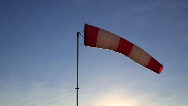 Veleta rayada de viento rojo y blanco contra un cielo azul claro . — Vídeo de stock