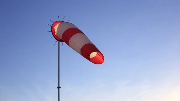 Gestreepte rode en witte windwijzer tegen een heldere blauwe hemel. — Stockvideo
