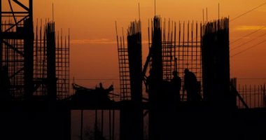 Konut bina inşaatı. İnşaatçılar bağlantı parçaları çıkıntılı bitmemiş yere gidin. Arka planda bir turuncu günbatımı işçilerin siluetleri.