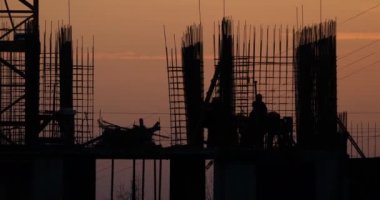 Konut bina inşaatı. İnşaatçılar bağlantı parçaları çıkıntılı bitmemiş yere gidin. Arka planda bir turuncu günbatımı işçilerin siluetleri.