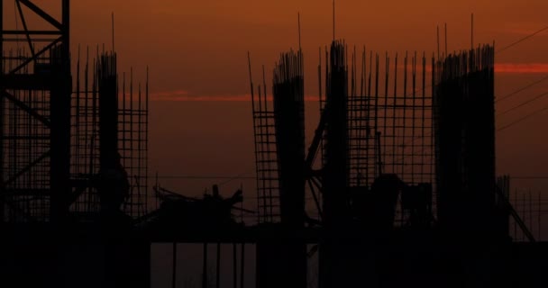 Construcción de un edificio residencial. Los constructores van en el piso sin terminar con accesorios sobresalientes. Siluetas de los trabajadores en el fondo de una puesta de sol naranja . — Vídeo de stock