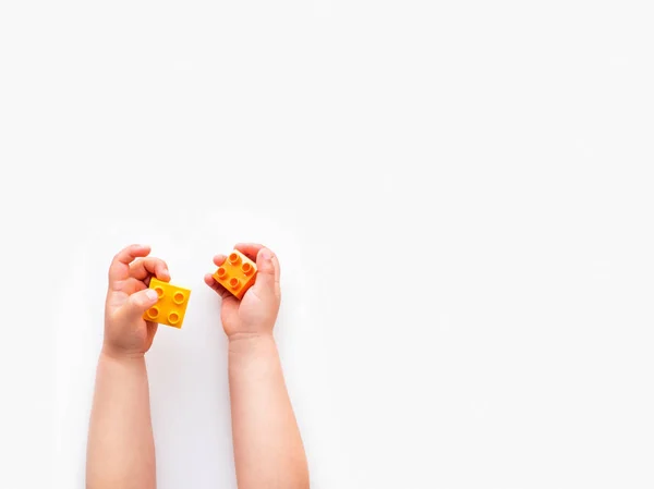 아이는 주먹에 오렌지와 파란색 생성자 블록holidng입니다. 흰색 배경에 벽돌 장난감 아이의 손. 교육 장난감, 평평, 상단 보기. — 스톡 사진