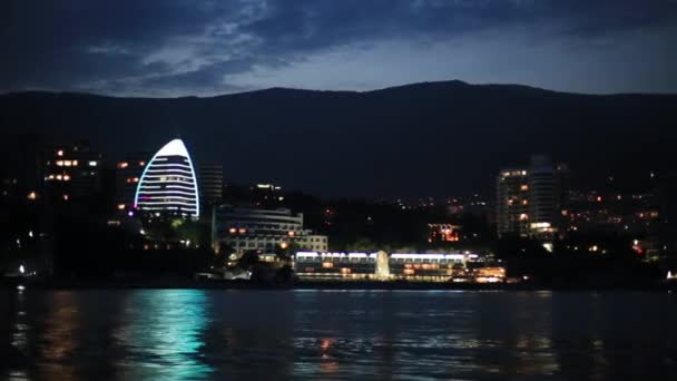 Panoráma kilátás a Yalta városba a Fekete-tengertől. Éjszakai élet a rakparton. Kilátás mozgó csónakot. Krím — Stock videók
