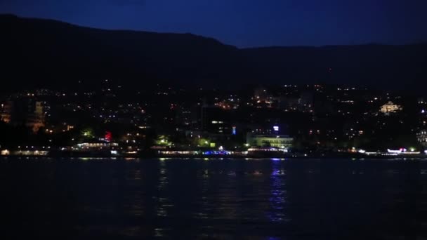 Panoráma kilátás a Yalta városba a Fekete-tengertől. Éjszakai élet a rakparton. Kilátás mozgó csónakot. Krím — Stock videók