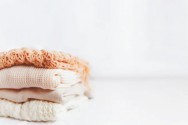 Pile of beige woolen clothes on a white background. Warm knitted sweaters and scarfs are folded in one heap. Place for text. — Stock Photo, Image