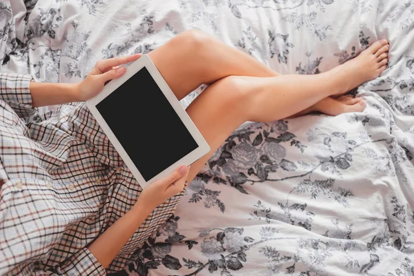 Женщина в клетчатой рубашке сидит на кровати с планшетом. Уютное утро дома. Время спать с гаджетом . — стоковое фото