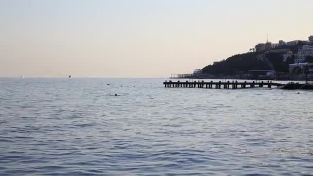 黒い海で泳いでいる人々。ヤルタの町の海辺の冬の夕日。クリミア. — ストック動画