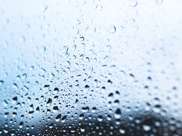 Rain drops on glass. Silhouettes of water drops on blue transparent surface.