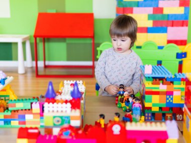 Ufaklık renkli inşaatçıyla çocuk odasında oynuyor. Elinde eğitici oyuncak bloğu vardı. Çocuk oyuncak tuğlalarla meşgul..