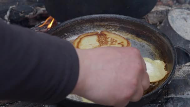 Турист готовит блинчики на сковородке над огнем. Костер в лесу . — стоковое видео