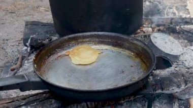 Turist ateşin üzerinde tavada krep pişiriyor. Ormanda kamp ateşi.