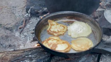 Turist ateşin üzerinde tavada krep pişiriyor. Ormanda kamp ateşi.