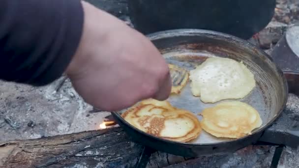 El turista está cocinando panqueques en una sartén sobre el fuego. Hoguera en el bosque . — Vídeo de stock