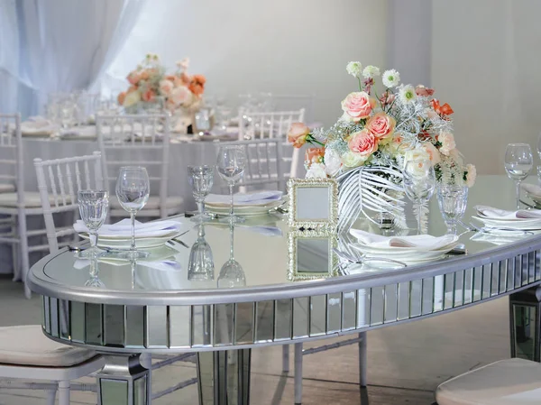 Mesa servida para banquete de bodas con cubiertos y flores en jarrones. Gafas y espejos transparentes como decoración . — Foto de Stock