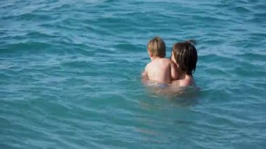 Oğlu denizde yüzen baba. Yeni yürümeye başlayan adam su dalgalarında oynuyor. Aile eğlence aktivitesi.