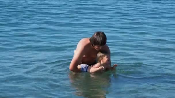 Vater und Sohn schwimmen im Meer. Mann mit Kleinkind spielen in Wasserwellen. Freizeitaktivitäten für Familien. — Stockvideo