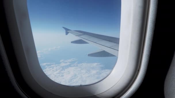 View on blue sky and fluffy white clouds through the window of the aircraft. Scenic view from flying airplane. — Stock Video