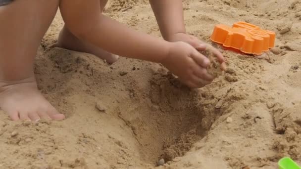 Menino está brincando com areia e moldes em caixa de areia. Caminhadas de bebê com os pés descalços no parque infantil. Atividades de lazer ao ar livre ,. — Vídeo de Stock