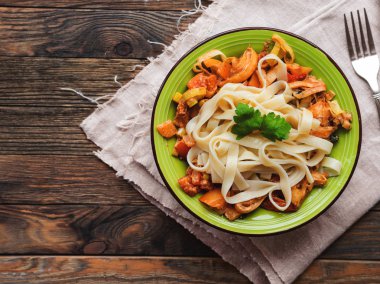 Lezzetli fettuccine ve domates sosu ile yeşil plaka. Ahşap masa, peçete ve makarna ile kase üst görünümü. İtalyan mutfağı.