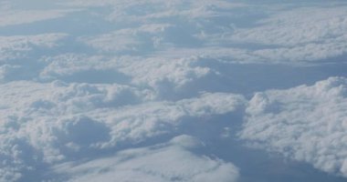 Uçağın penceresinden mavi gökyüzü ve kabarık beyaz bulutlar görünümü. Uçan uçaktan manzara.