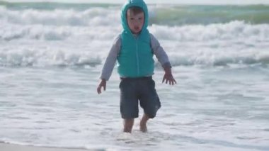 Yelekli çocuk deniz kenarındaki kumla oynuyor..