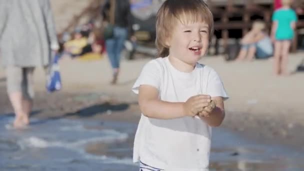 Leksakspojken i badkläder leker med sand på havssidan.. — Stockvideo