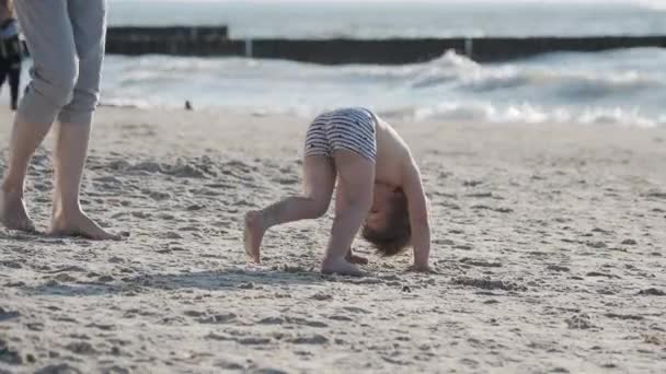 Niño pequeño en traje de baño está jugando con arena en el lado del mar . — Vídeos de Stock