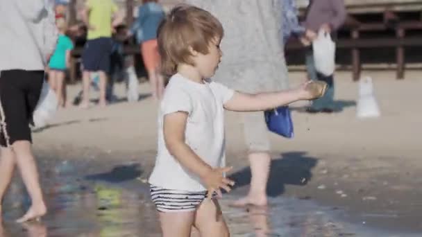 Niño pequeño en traje de baño está jugando con arena en el lado del mar . — Vídeos de Stock