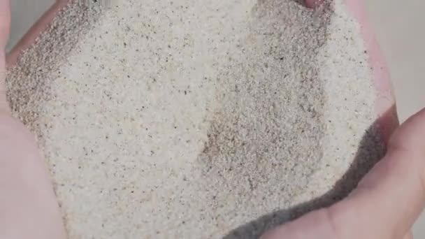 砂が指を通って注ぐ。女性は砂浜で砂遊びをしている。時の象徴. — ストック動画