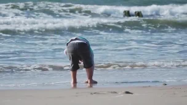 Menino de colete está brincando com areia no lado do mar . — Vídeo de Stock