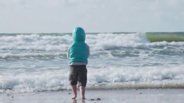 Yelekli çocuk deniz kenarındaki kumla oynuyor..