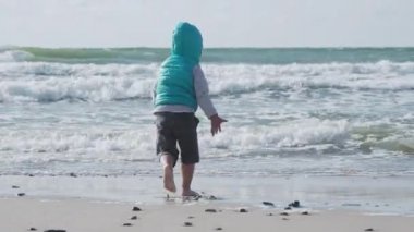 Yelekli çocuk deniz kenarındaki kumla oynuyor..