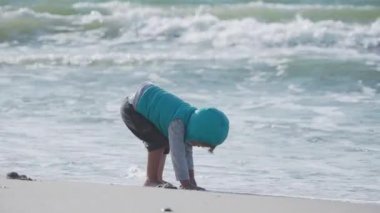 Yelekli çocuk deniz kenarındaki kumla oynuyor..