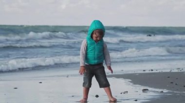 Yelekli çocuk deniz kenarındaki kumla oynuyor..