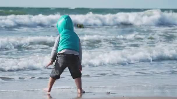 Leksakspojken i väst leker med sand på havssidan.. — Stockvideo