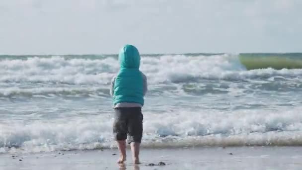 A kisgyerek mellényben homokkal játszik a tenger oldalán.. — Stock videók