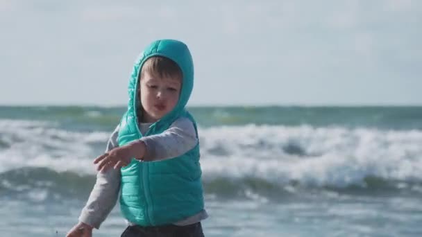 Toddler boy in waistcoat is playing with sand on sea side. — Stock Video