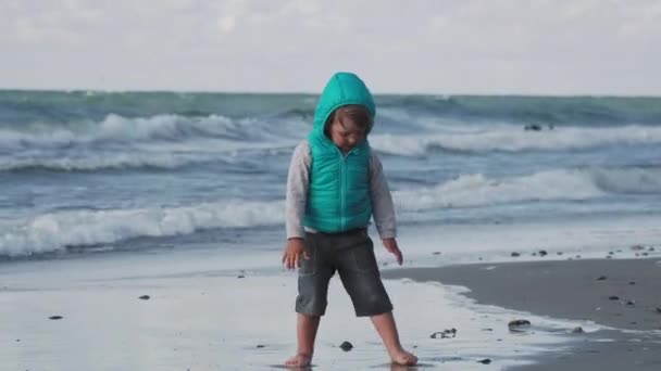 Menino de colete está brincando com areia no lado do mar . — Vídeo de Stock