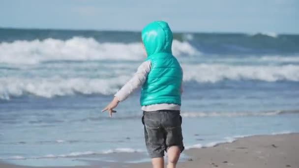 Niño pequeño en chaleco está jugando con arena en el lado del mar . — Vídeo de stock