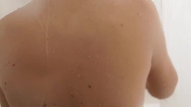 Çıplak kadın duş alıyor. Kadın kısa saçlarını suyla yıkıyor. Beyaz banyoda yavaş çekim videosu.