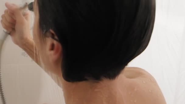 Meztelen nő zuhanyozik. A nő vízzel mossa a rövid haját. Lassított mozgású videó fehér fürdőszobában. — Stock videók