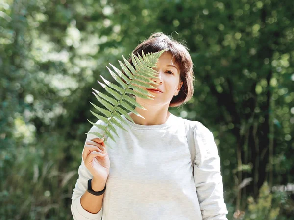 若い女性がシダの葉で目を隠している 生命の象徴 自然との静けさと統一 夏の森 — ストック写真