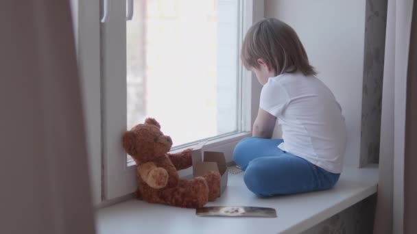 Toddler ül az ablakpárkányon, és játszik szóró tabletták nélkül szülők ellenőrzése. Veszélyes helyzet a kisfiúval. A gyógyszerek szabadon hozzáférhetőek a gyermekek számára.. — Stock videók