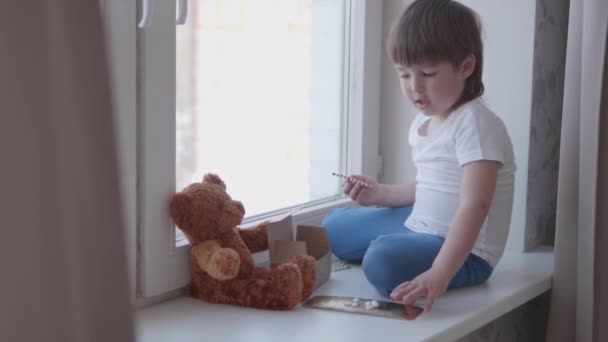 Toddler sitter på fönsterbrädan och leker med spridningspiller utan föräldrakontroll. Farlig situation med lille pojken. Läkemedel är fritt tillgängliga för barn. — Stockvideo