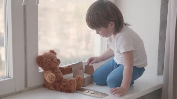 Kleinkind sitzt auf Fensterbank und spielt ohne Kontrolle der Eltern mit Streupillen. Gefährliche Situation mit kleinem Jungen. Medikamente sind für Kinder frei verfügbar. — Stockvideo