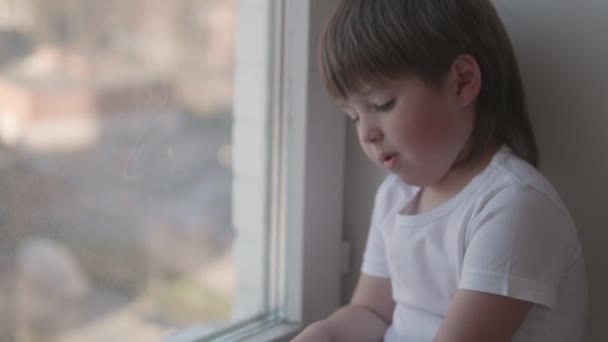 Kleinkind sitzt auf Fensterbank und spielt ohne Kontrolle der Eltern mit Streupillen. Gefährliche Situation mit kleinem Jungen. Medikamente sind für Kinder frei verfügbar. — Stockvideo