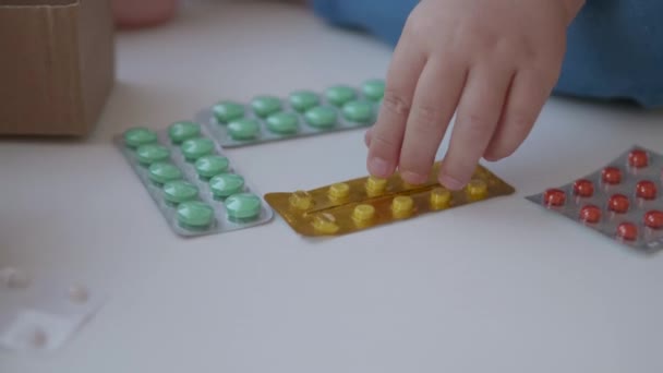 El niño se sienta en el alféizar de la ventana y juega con píldoras de dispersión sin control de los padres. Una situación peligrosa con un niño pequeño. Los medicamentos están disponibles gratuitamente para los niños . — Vídeo de stock