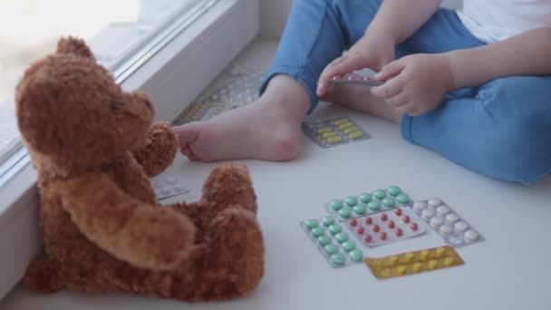 Toddler ül az ablakpárkányon, és játszik szóró tabletták nélkül szülők ellenőrzése. Veszélyes helyzet a kisfiúval. A gyógyszerek szabadon hozzáférhetőek a gyermekek számára.. — Stock videók