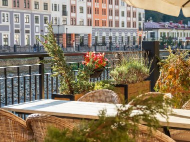 Mzymta nehir kıyısındaki kafede masa, sandalye ve saksı ağaçları. Rosa Dolina 'nın temiz ve bakımlı sokakları, Soçi, Rusya yakınlarındaki ünlü Rosa Khutor Alpine Kayak Resort' un bir parçası..