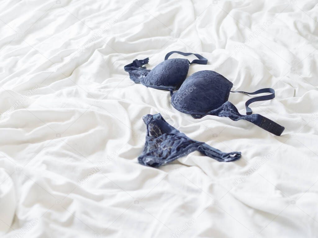 Deep blue laced bra and thong. Elegant underwear on white crumpled bed sheet. Unmade bed at morning. Getting ready at cozy home.